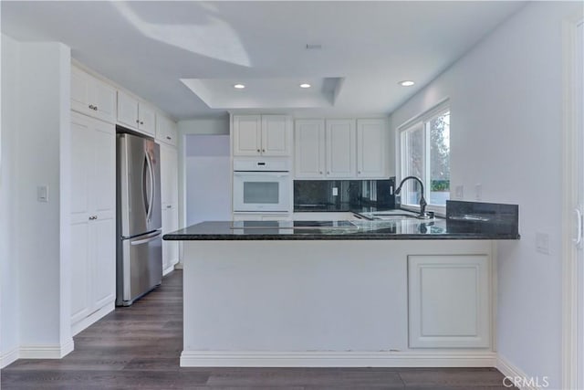 kitchen featuring white oven, white cabinets, stainless steel fridge, and kitchen peninsula