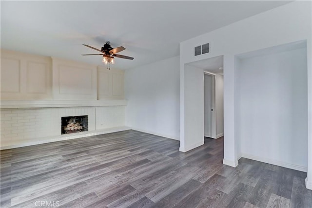 unfurnished living room with dark wood-type flooring, a brick fireplace, and ceiling fan