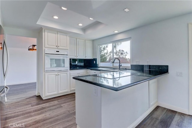 kitchen with kitchen peninsula, sink, a tray ceiling, white appliances, and white cabinets