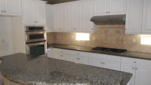 kitchen with dark stone counters, decorative backsplash, appliances with stainless steel finishes, range hood, and white cabinetry