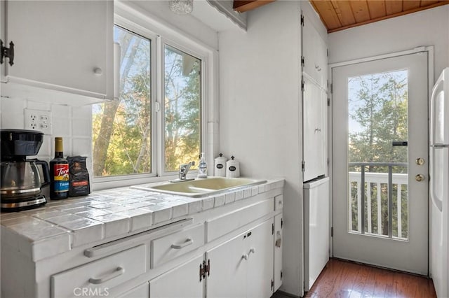 kitchen with a wealth of natural light, wood ceiling, sink, white cabinetry, and tile counters