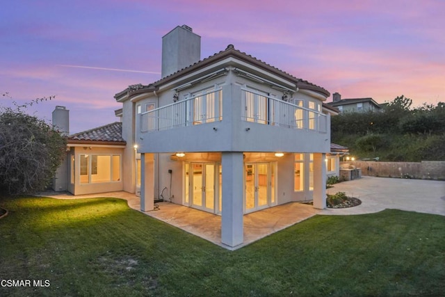 back house at dusk featuring a patio area, a balcony, and a yard