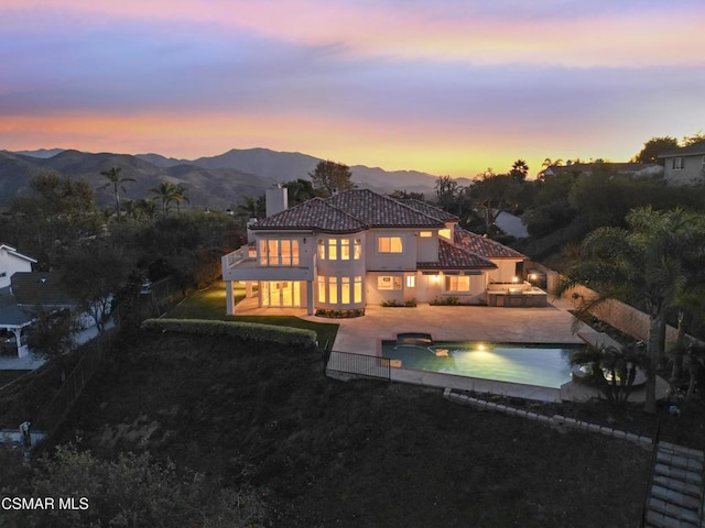 back house at dusk featuring a balcony, a patio, a fenced in pool, a mountain view, and a yard