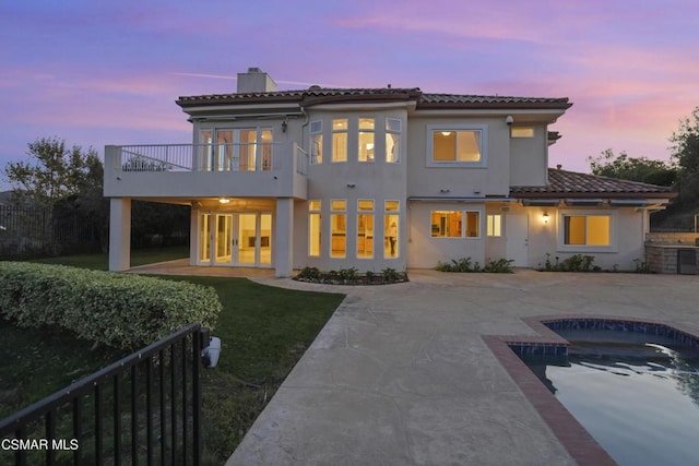 back house at dusk featuring a balcony and a patio