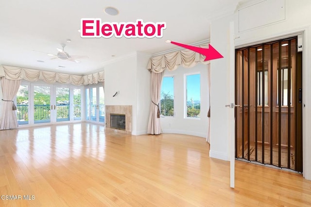 unfurnished living room with ceiling fan, light wood-type flooring, a tile fireplace, and crown molding