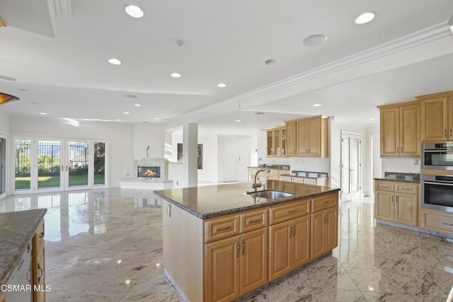 kitchen with dark stone countertops, a kitchen island with sink, ornamental molding, double oven, and sink