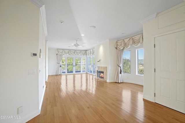 unfurnished living room featuring ceiling fan, light wood-type flooring, ornamental molding, and a fireplace