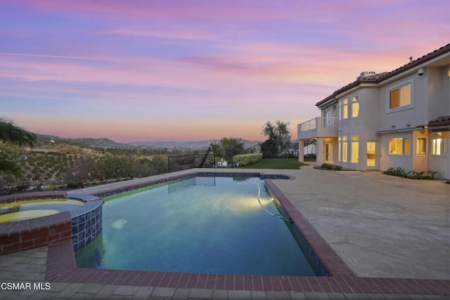 pool at dusk with a patio area and an in ground hot tub