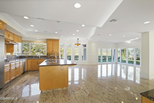 kitchen featuring dark stone countertops, a kitchen island with sink, backsplash, ornamental molding, and sink