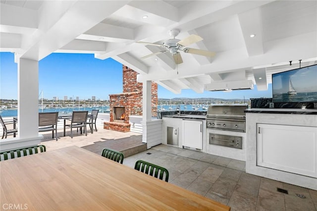 view of patio with an outdoor kitchen, an outdoor brick fireplace, ceiling fan, a water view, and grilling area