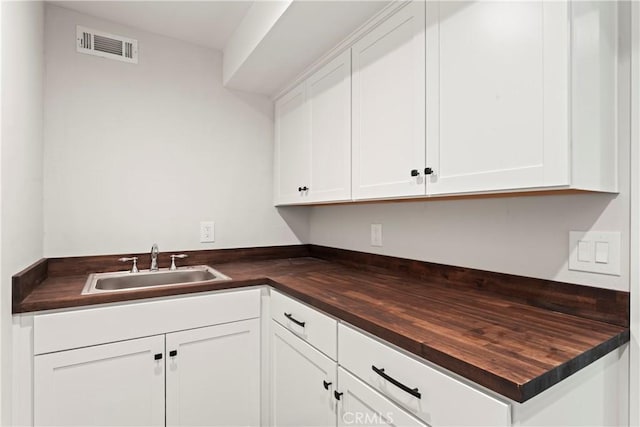 kitchen with butcher block countertops, sink, and white cabinets