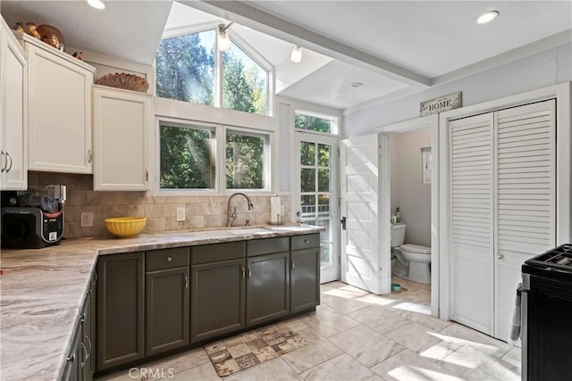 kitchen with decorative backsplash, light stone countertops, sink, white cabinetry, and range with electric stovetop