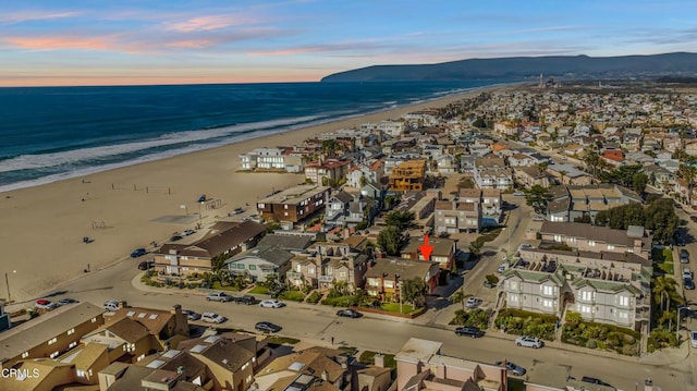 aerial view at dusk featuring a water view and a beach view