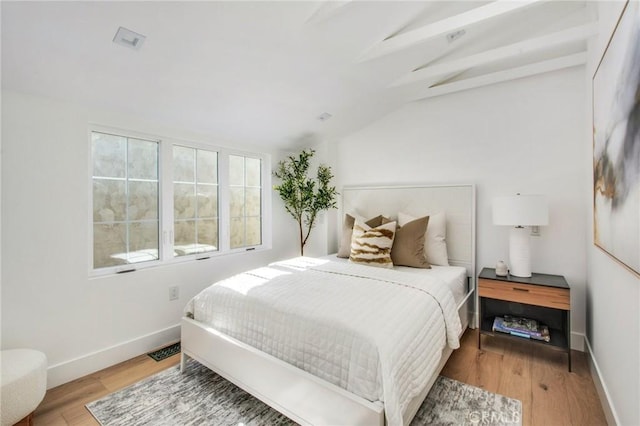 bedroom featuring vaulted ceiling with beams and light hardwood / wood-style flooring