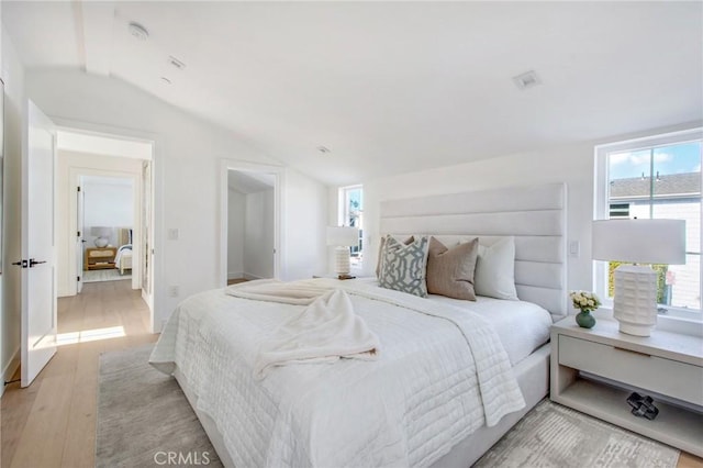 bedroom with multiple windows, vaulted ceiling, and light wood-type flooring