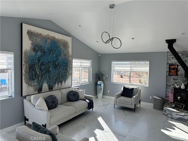 living area featuring vaulted ceiling, marble finish floor, a wood stove, and baseboards