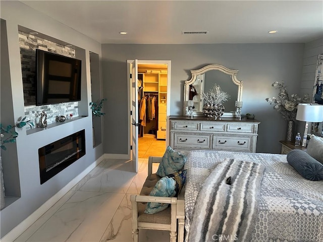 bedroom with a walk in closet, marble finish floor, recessed lighting, visible vents, and a glass covered fireplace