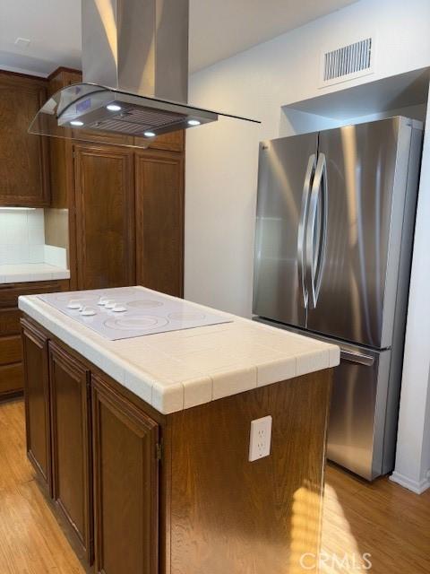 kitchen featuring island range hood, stainless steel fridge, a center island, and tile countertops