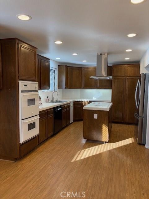 kitchen with double oven, black dishwasher, wall chimney exhaust hood, and light wood-type flooring