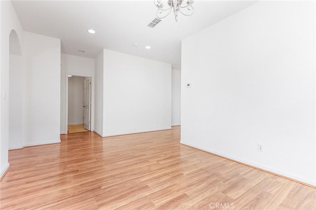 spare room featuring light wood-type flooring and a notable chandelier