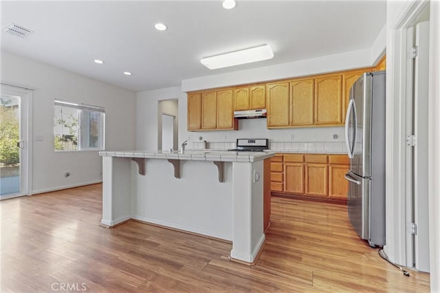 kitchen featuring white range, light wood-type flooring, a kitchen island with sink, and stainless steel refrigerator