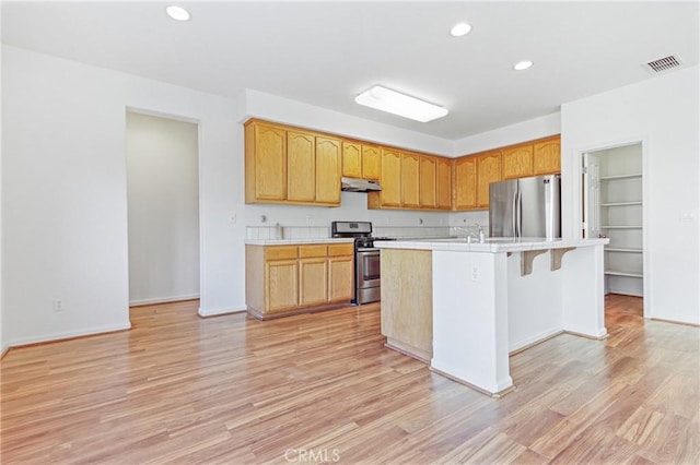 kitchen featuring light wood-type flooring, stainless steel appliances, a breakfast bar area, and an island with sink