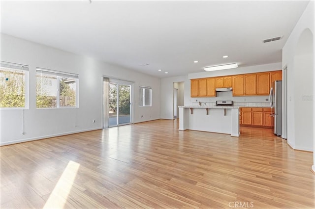 kitchen with a kitchen island, a kitchen bar, light wood-type flooring, and stainless steel appliances