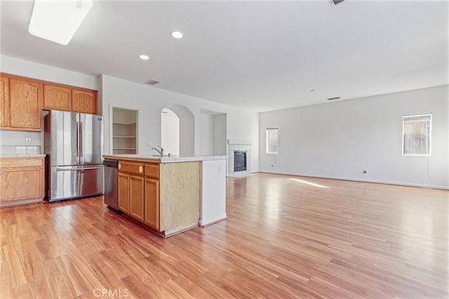 kitchen with sink, light hardwood / wood-style flooring, a tiled fireplace, a kitchen island with sink, and appliances with stainless steel finishes