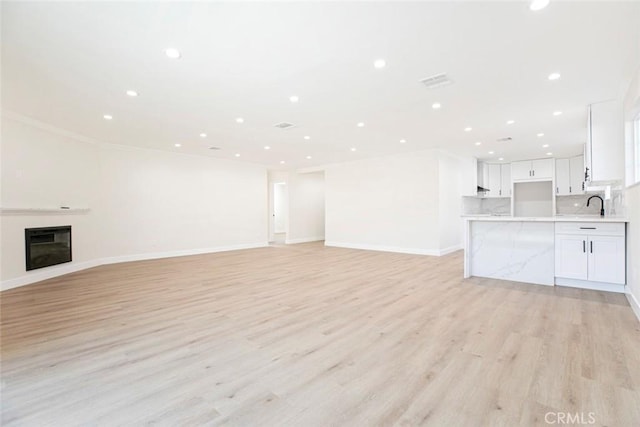 unfurnished living room featuring sink and light hardwood / wood-style floors