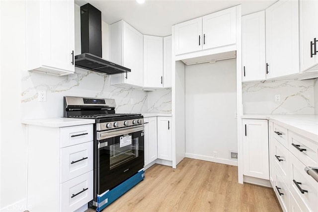 kitchen with stainless steel gas stove, light stone counters, light hardwood / wood-style floors, white cabinets, and wall chimney exhaust hood