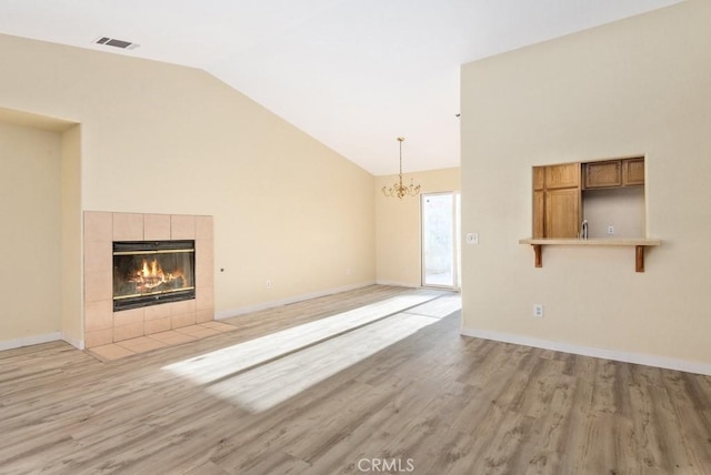 unfurnished living room featuring light wood-type flooring, a fireplace, high vaulted ceiling, and a chandelier