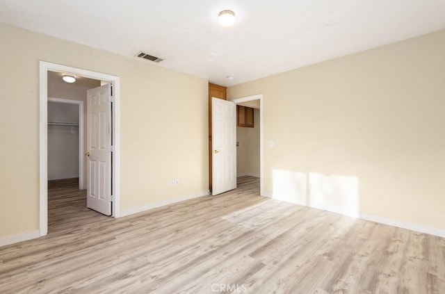 unfurnished bedroom featuring a closet, a walk in closet, and light hardwood / wood-style flooring