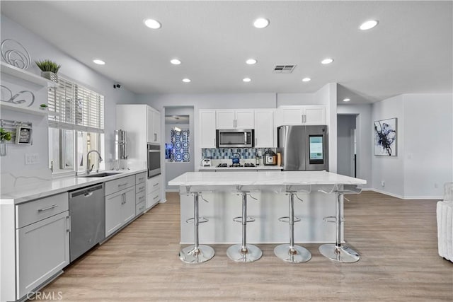 kitchen with sink, a center island, light hardwood / wood-style flooring, white cabinets, and appliances with stainless steel finishes