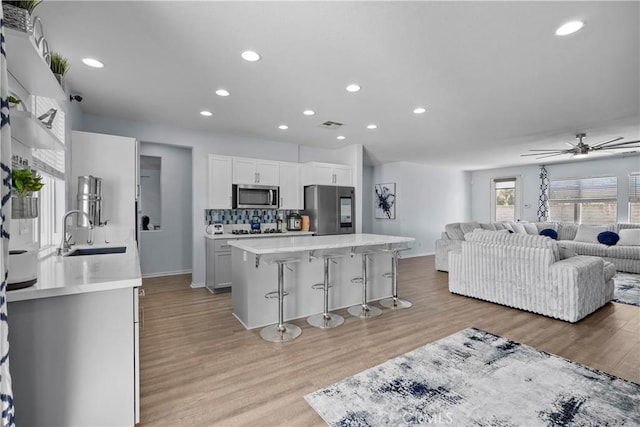 kitchen featuring white cabinetry, sink, stainless steel appliances, a breakfast bar, and light wood-type flooring