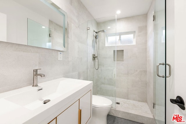 bathroom with vanity, a shower with door, backsplash, toilet, and tile walls