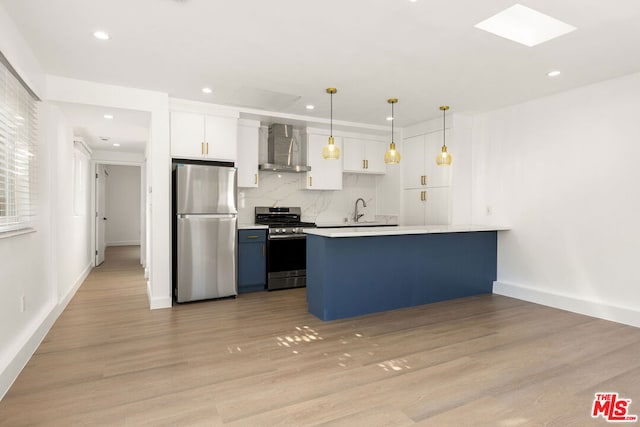 kitchen with pendant lighting, wall chimney range hood, light hardwood / wood-style floors, white cabinetry, and stainless steel appliances