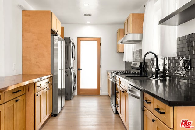 kitchen with sink, decorative backsplash, light wood-type flooring, stacked washing maching and dryer, and appliances with stainless steel finishes