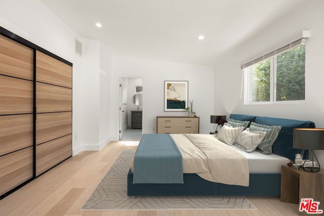 bedroom featuring light wood-type flooring, ensuite bathroom, and lofted ceiling