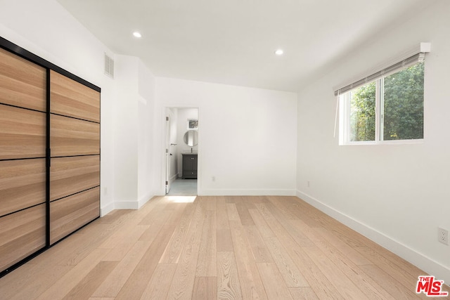 unfurnished bedroom featuring ensuite bathroom and light hardwood / wood-style floors