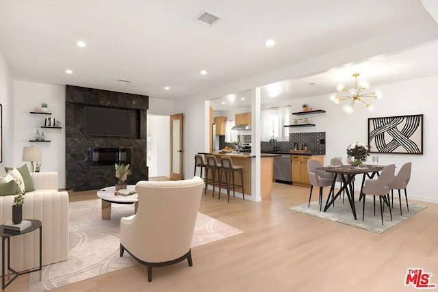 living room featuring sink, light wood-type flooring, a fireplace, and an inviting chandelier