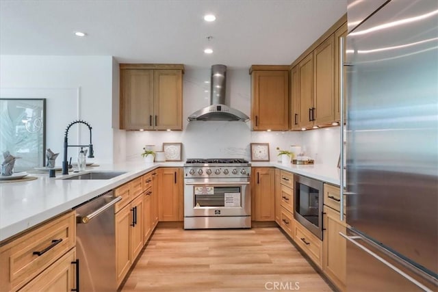 kitchen with built in appliances, sink, light hardwood / wood-style floors, and wall chimney range hood