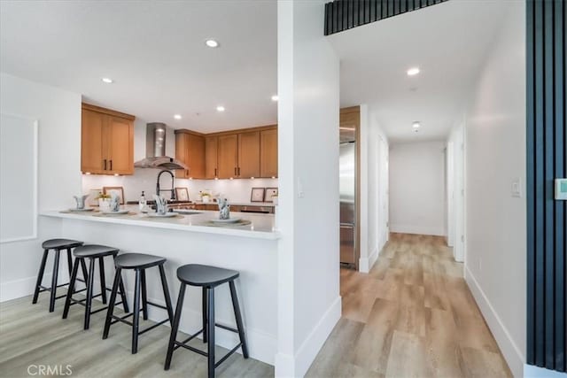 kitchen featuring kitchen peninsula, a kitchen bar, wall chimney exhaust hood, sink, and light hardwood / wood-style flooring