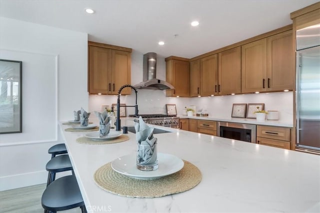 kitchen featuring beverage cooler, wall chimney range hood, a kitchen breakfast bar, built in fridge, and light hardwood / wood-style flooring