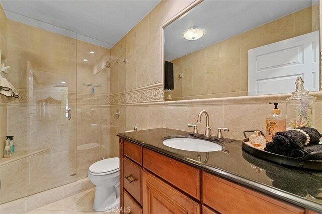 bathroom featuring tile patterned floors, toilet, a shower with door, vanity, and tile walls