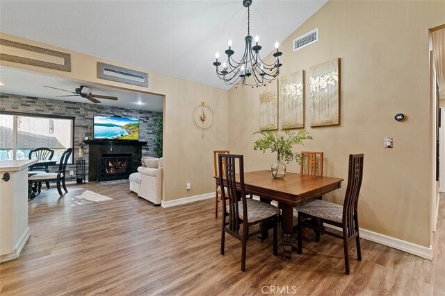 dining room featuring a fireplace, ceiling fan with notable chandelier, hardwood / wood-style flooring, and vaulted ceiling