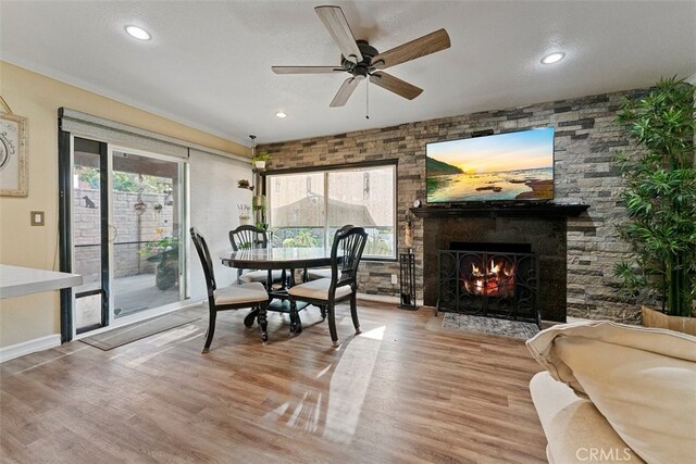 dining room with ceiling fan, a stone fireplace, light wood-type flooring, and a wealth of natural light