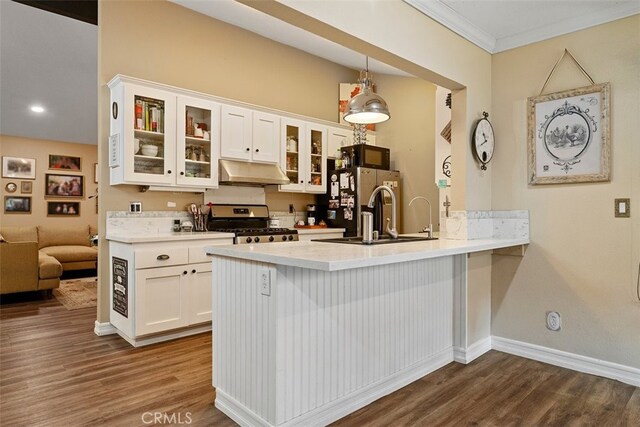 kitchen with dark wood-type flooring, stainless steel appliances, kitchen peninsula, white cabinets, and ornamental molding