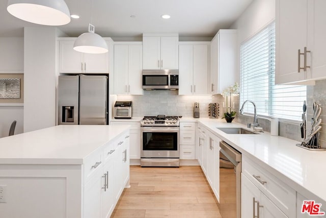 kitchen featuring sink, hanging light fixtures, stainless steel appliances, white cabinets, and light wood-type flooring