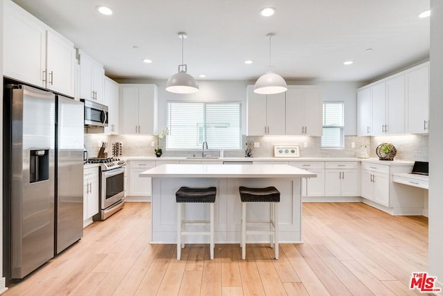 kitchen with pendant lighting, stainless steel appliances, white cabinetry, and a healthy amount of sunlight