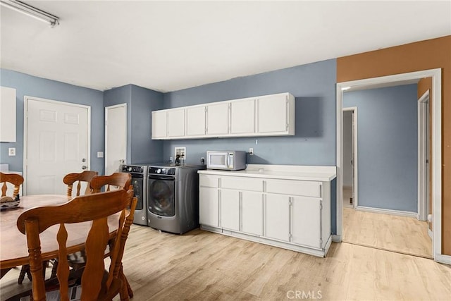 washroom with washing machine and dryer, light hardwood / wood-style flooring, and cabinets